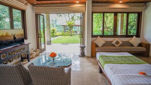 A room with a bed, a sofa, a coffee table, and a TV. There is a view of a garden outside. - The Allure Ubud Villas & Spa crafted by freshWater Asia (Ubud)