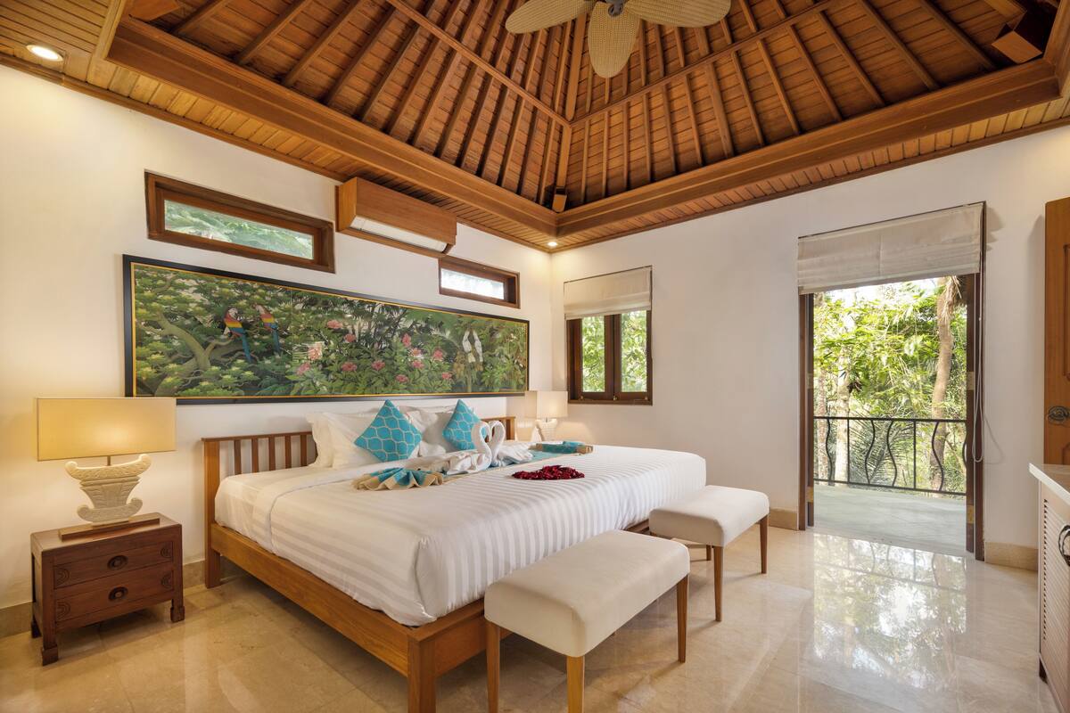 A spacious bedroom with a large bed, wooden headboard, and a view of the outdoors through a balcony.