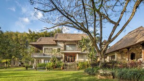A two-story house with a thatched roof, surrounded by lush greenery and a well-maintained lawn. - The Allure Ubud Villas & Spa crafted by freshWater Asia (Ubud)