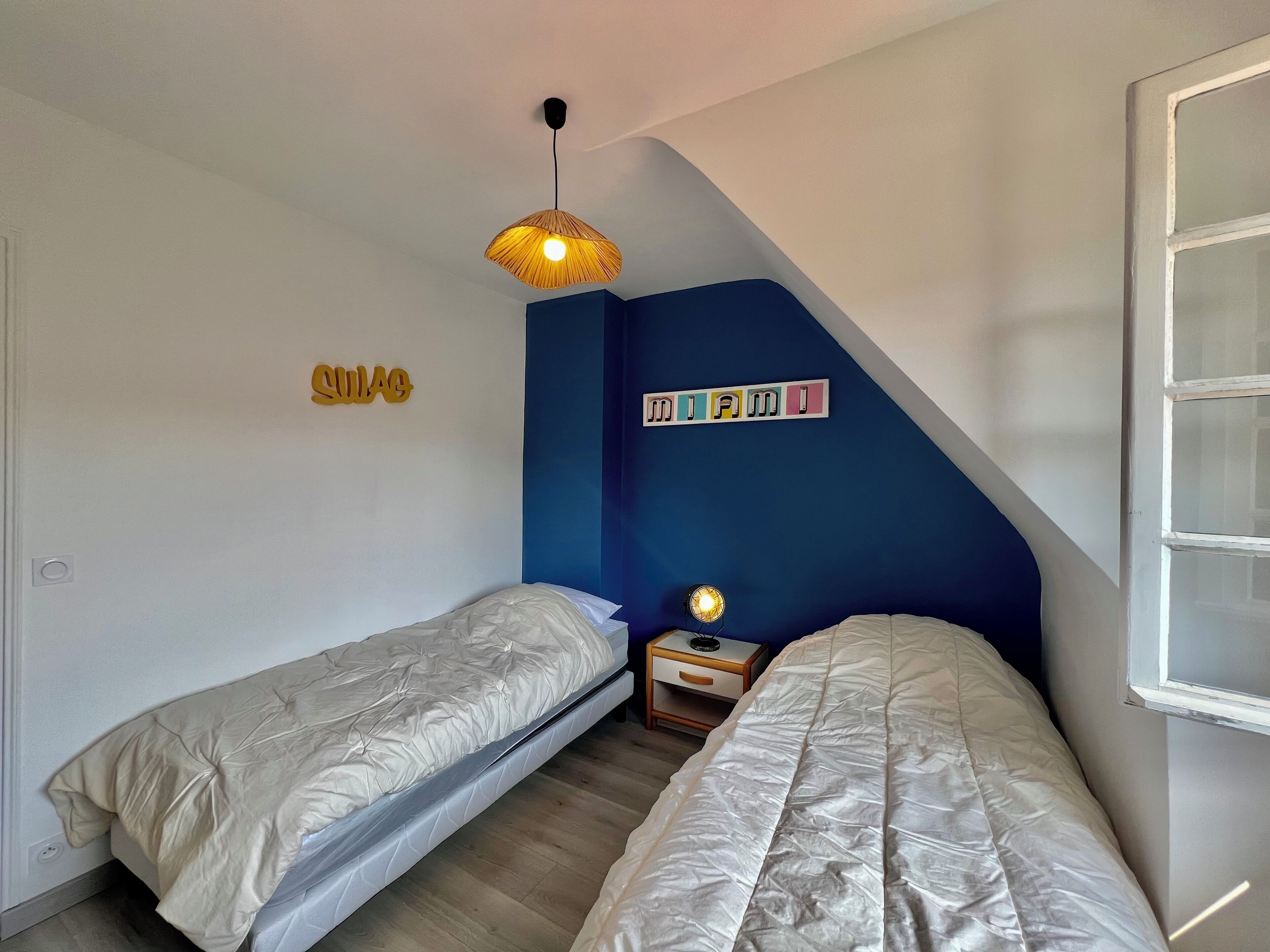 Un dormitorio con dos camas individuales, una mesita de noche con lámpara y una lámpara de techo.