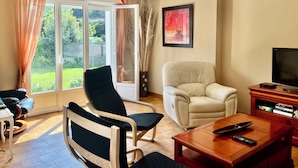 A living room with a sofa, armchairs, a coffee table, a TV, and a bookshelf. - La Roseraie-8P-Wifi-Jardin Clos (Quiberon)