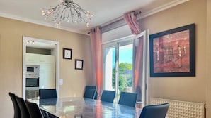 A dining area with a glass table, black chairs, a chandelier, and a painting on the wall. - La Roseraie-8P-Wifi-Jardin Clos (Quiberon)