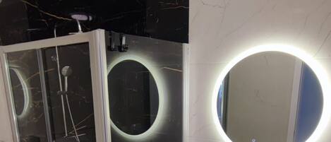 A modern bathroom with a glass shower enclosure, a round mirror, and a white sink.