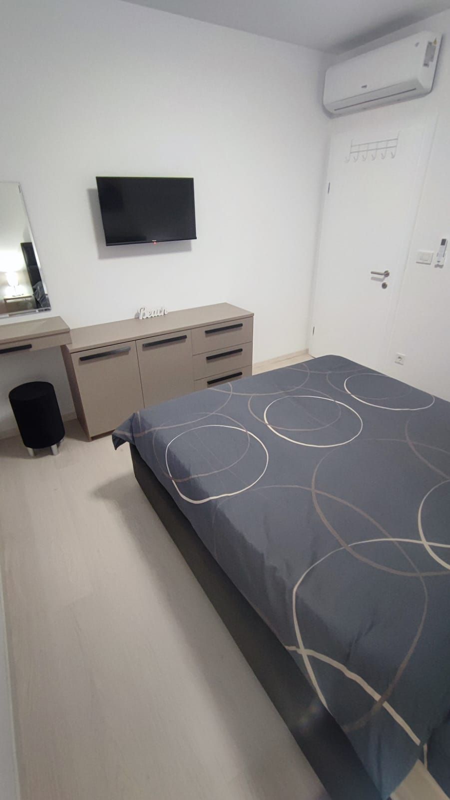 Ett sovrum med en säng, ett skrivbord, en stol, en spegel och en tv.