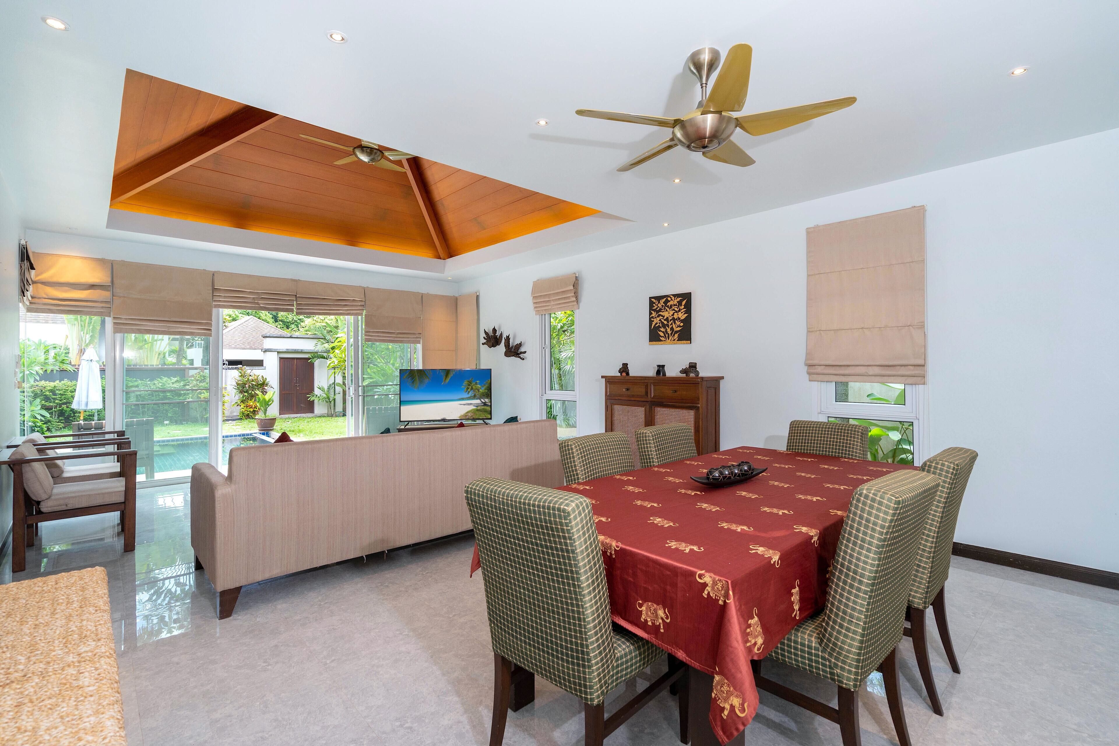 A dining area with a table set for four, surrounded by four chairs, a sofa, and a ceiling fan.