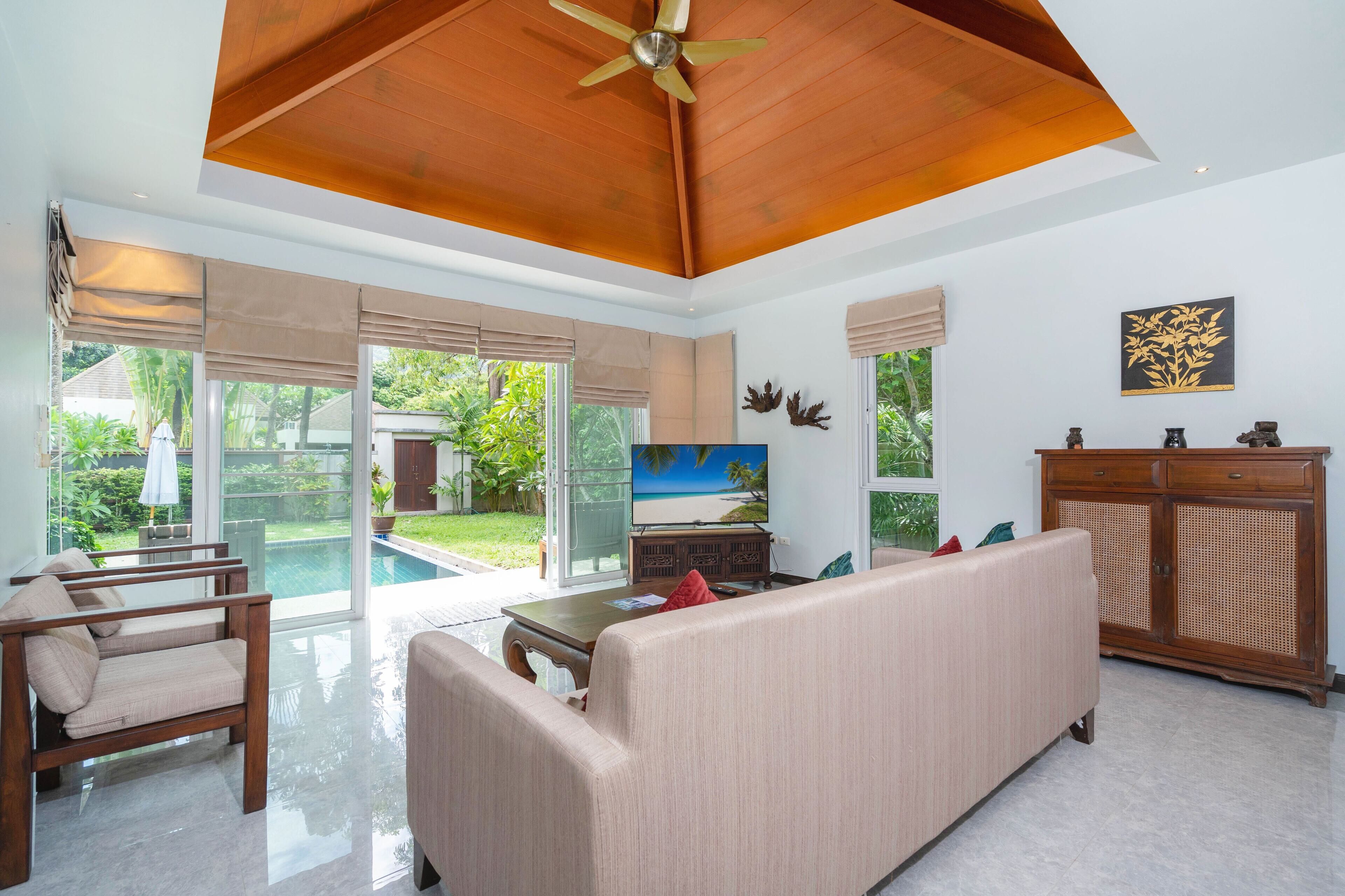 Amplia sala de estar con un televisor grande, asientos cómodos, ventilador de techo y vista a una piscina.