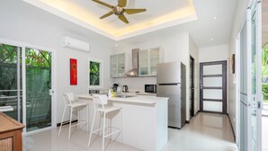 A modern kitchen with a central island, white bar stools, and a ceiling fan. - Tropical 3BR Pool Villa Morning Forest  (Rawai)