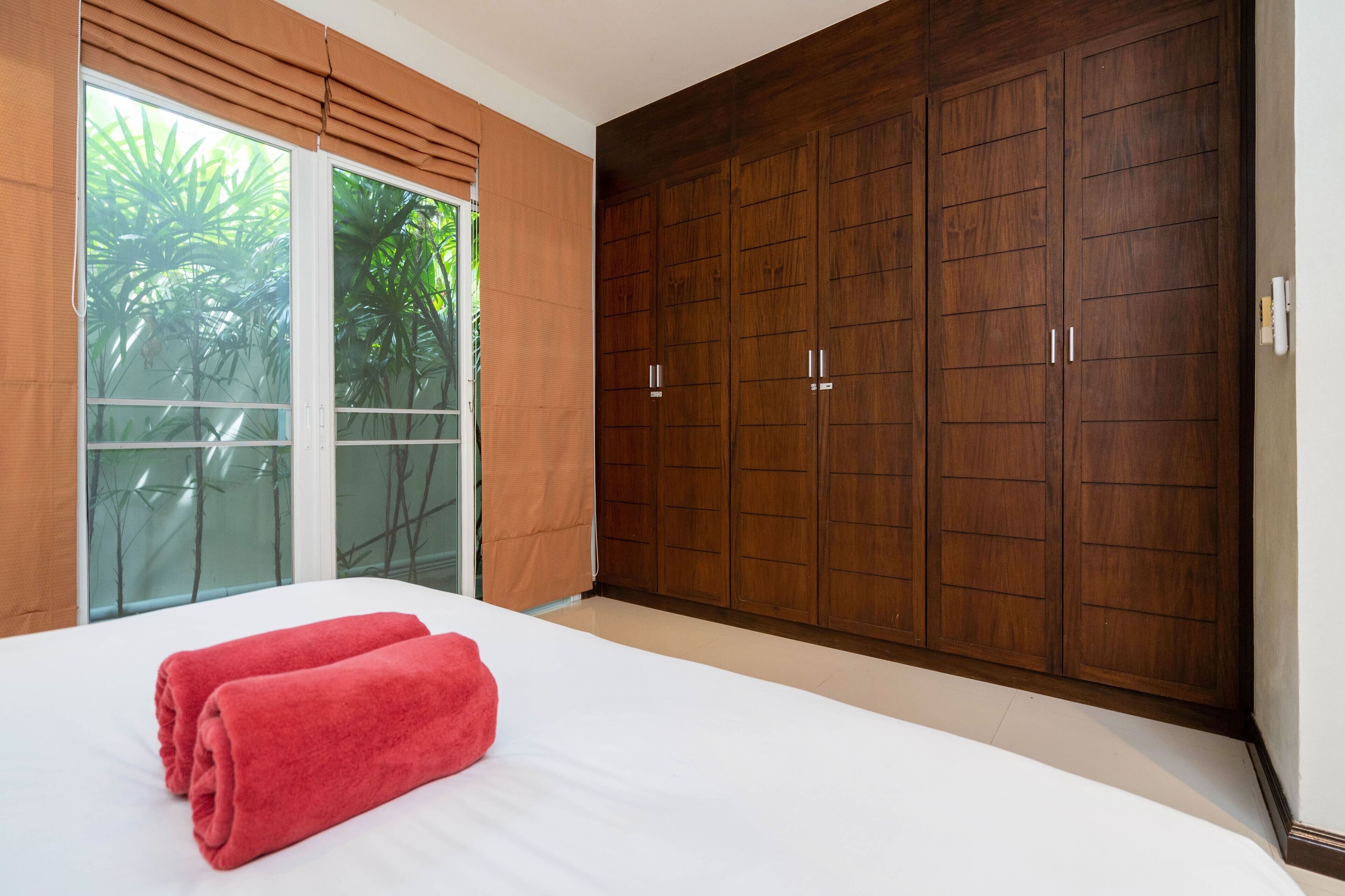 A bedroom with a large bed, a sliding glass door to a balcony, and a wooden wardrobe.