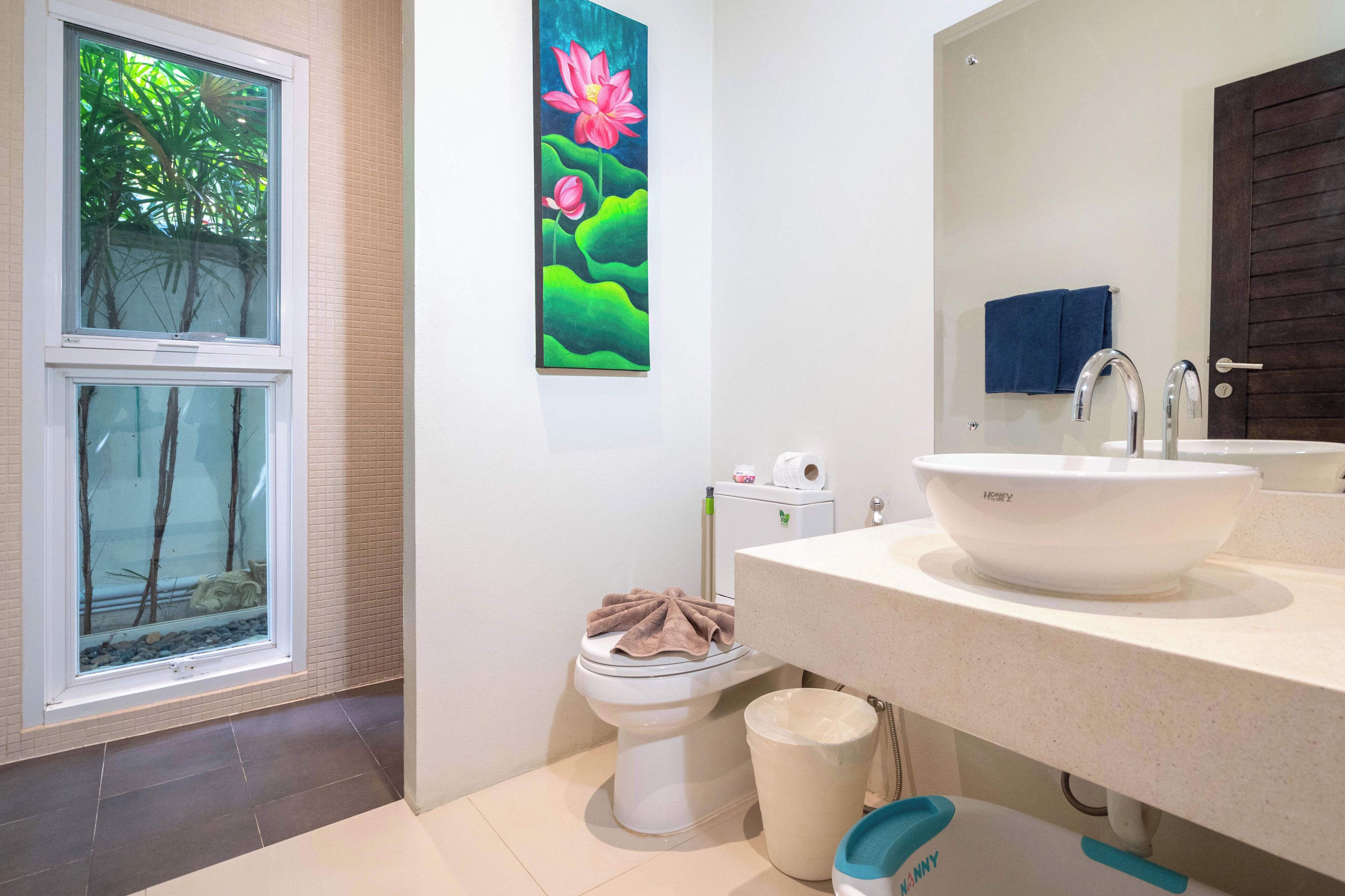 A bathroom with a large window, a toilet, a sink, and a mirror.