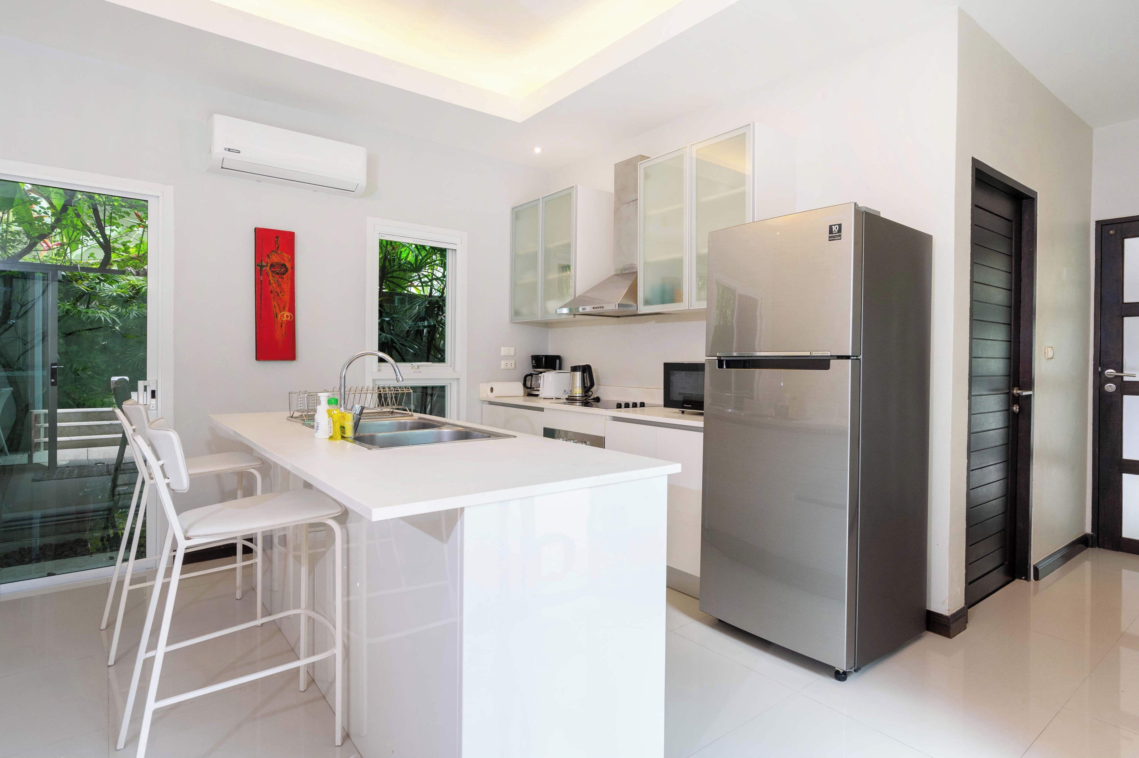 A modern kitchen with a large island, stainless steel appliances, and a glass door leading to an outdoor area.