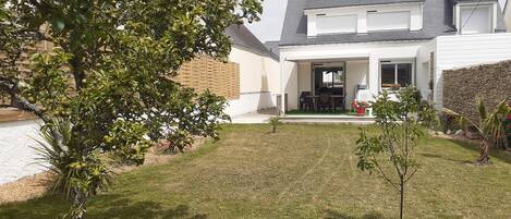 Une maison moderne dotée d’un patio couvert, d’une petite pelouse et d’un arbre fruitier.