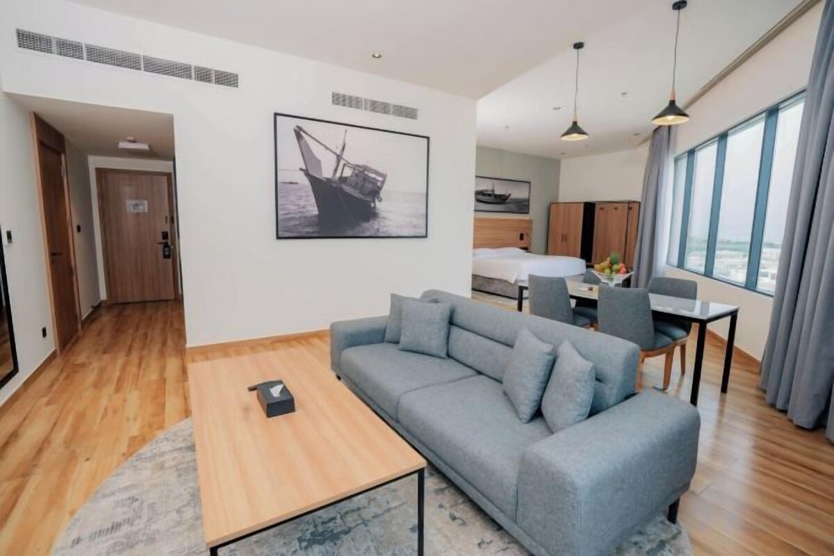 Een moderne hotelkamer met een bank, een eettafel, een kitchenette en een groot raam.