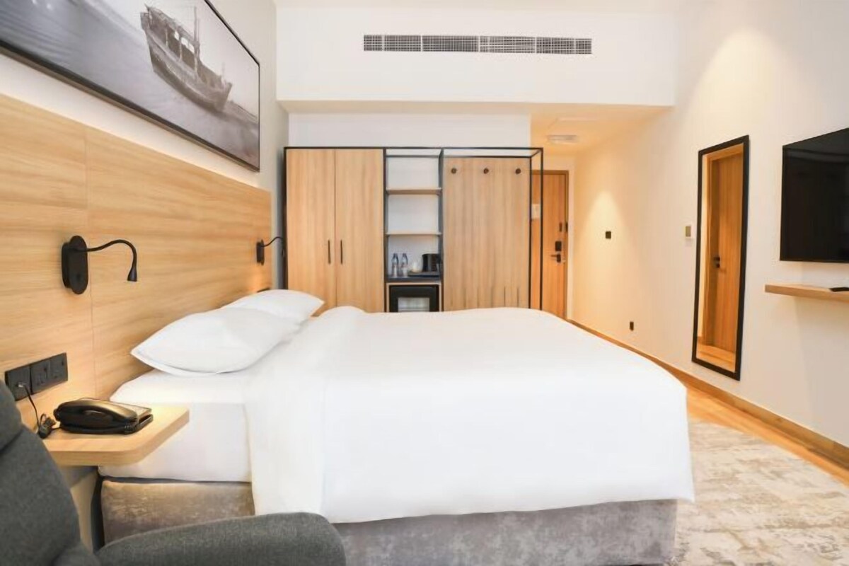 Une chambre d’hôtel moderne équipée d’un lit, d’un bureau avec un téléphone, d’une télévision et d’une armoire.