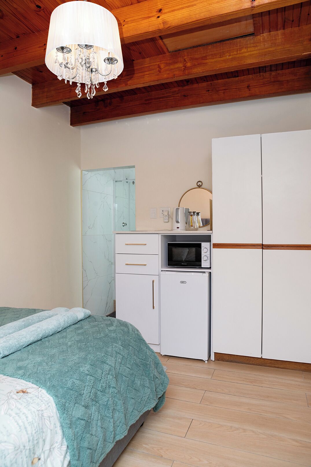 Un dormitorio con una cama, un pequeño rincón americano, un armario blanco y techo de madera.