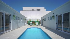 A swimming pool with two lounge chairs and a small garden area in the center. - A peaceful and safe area, just minutes from the beach, bars, and restaurants. (Cape Town)