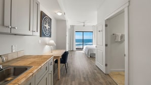 A modern kitchen with a wooden countertop and a dining area. A large window offers a view of the ocean.