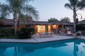 A residential property with a swimming pool, outdoor seating, and a well-lit patio area.
