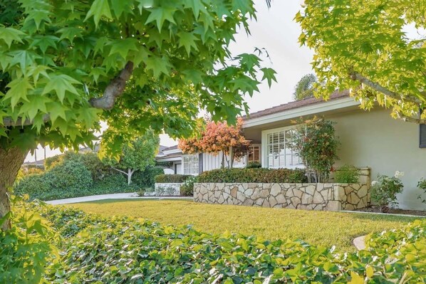 A residential house with a stone wall, a well-maintained lawn, and a large tree in the foreground. - @ Marbella Lane - Serene Ranch Style Home W/pool (Fullerton)
