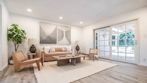 Un salon spacieux avec un canapé beige, une table basse et une grande fenêtre donnant sur un paysage verdoyant.