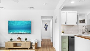 Una cocina moderna con armarios blancos, lavavajillas integrado y un televisor de pantalla plana grande montado en la pared.