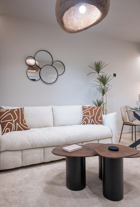 Una sala moderna con un sofá, dos mesas auxiliares, un elemento decorativo en la pared y una planta en maceta.