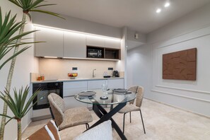 Una cocina moderna con armarios blancos, un microondas y una mesa de comedor de vidrio con cuatro sillas.