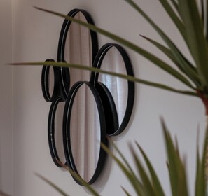 A wall-mounted black circular object, possibly a decorative piece or a functional item, with a plant partially visible in the foreground.