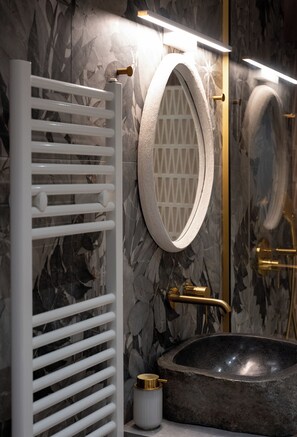 Un baño con un espejo redondo, un toallero blanco, un lavabo negro y una zona de ducha.