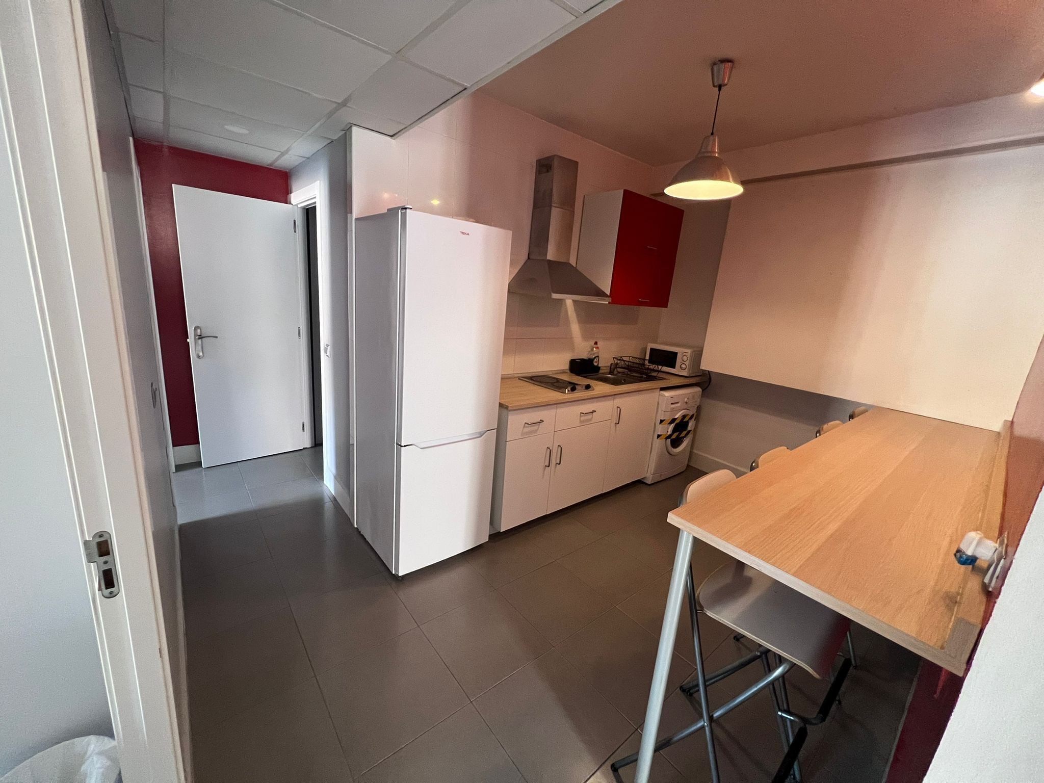 A compact kitchen with a refrigerator, microwave, and a wooden table.