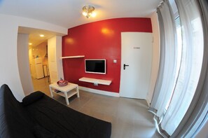 Un salon avec un mur d’accent rouge, un téléviseur à écran plat fixé au-dessus d’une console blanche et un canapé noir.