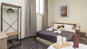 Une chambre d’hôtel comprenant un lit, une table de chevet, une armoire, une fenêtre avec des rideaux, un tableau au mur et une petite table de nuit avec une lampe.