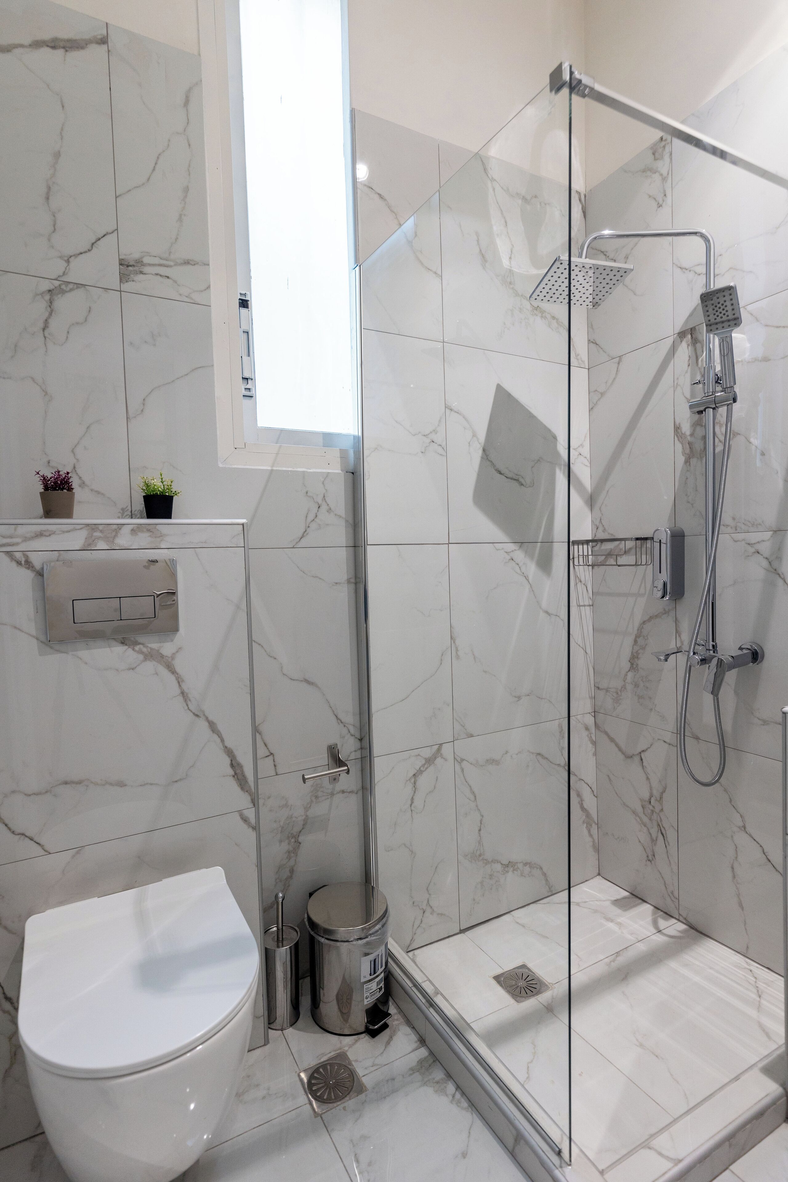 A modern bathroom with a glass-enclosed shower, a toilet, and marble tiles.