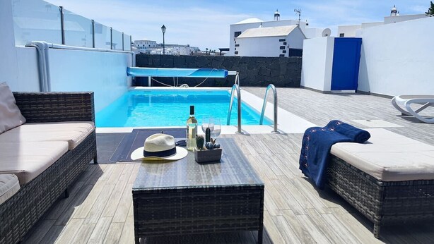 A rooftop pool area with wicker furniture, a bottle, and a hat on the deck. - Casa del Sol, heated pool quiet place (Playa Blanca)