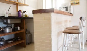 A kitchen with a wooden countertop, shelves, and a gas stove. There are stools and a chair near the counter. - Seasonal Apartment in Buzios - RJ (Armação dos Búzios)