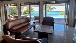 A modern living room with a leather sofa, a coffee table, and a view of the ocean through large windows. - Mokusiga Villas Tolu - Private Beachfront Villa (Korolevu)