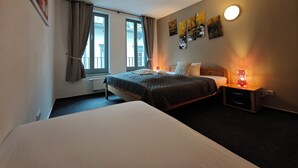 Et hotelværelse med en seng, et natbord med lampe, et vindue med gardiner og en væg med billeder i rammer.