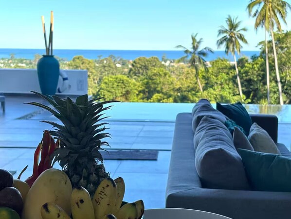 Un salón moderno con vista al océano, una piña y plátanos sobre la mesa.
