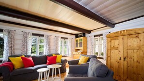 A cozy living room with a dark grey sofa, a smaller grey armchair, and a white coffee table. There are floral curtains on the windows, a wooden cabinet, and a large wooden door. - Beautiful private villa for 6 guests with WIFI, TV and terrace (Jablonec Nad Nisou)
