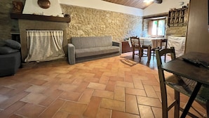 A cozy living room with a stone wall, a fireplace, a sofa, and a dining area with a table and chairs. - Locanda di Federico (Casteldelci)