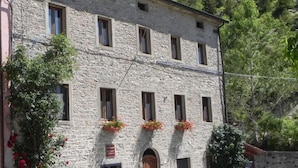 A stone building with a central entrance, multiple windows, and flower boxes on the second floor. - Locanda di Federico (Casteldelci)