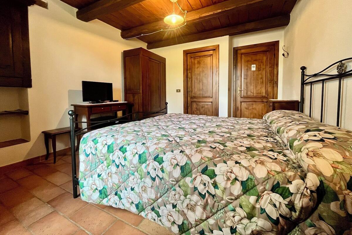 A bedroom with a floral bedspread, wooden wardrobe, and a television on a desk.
