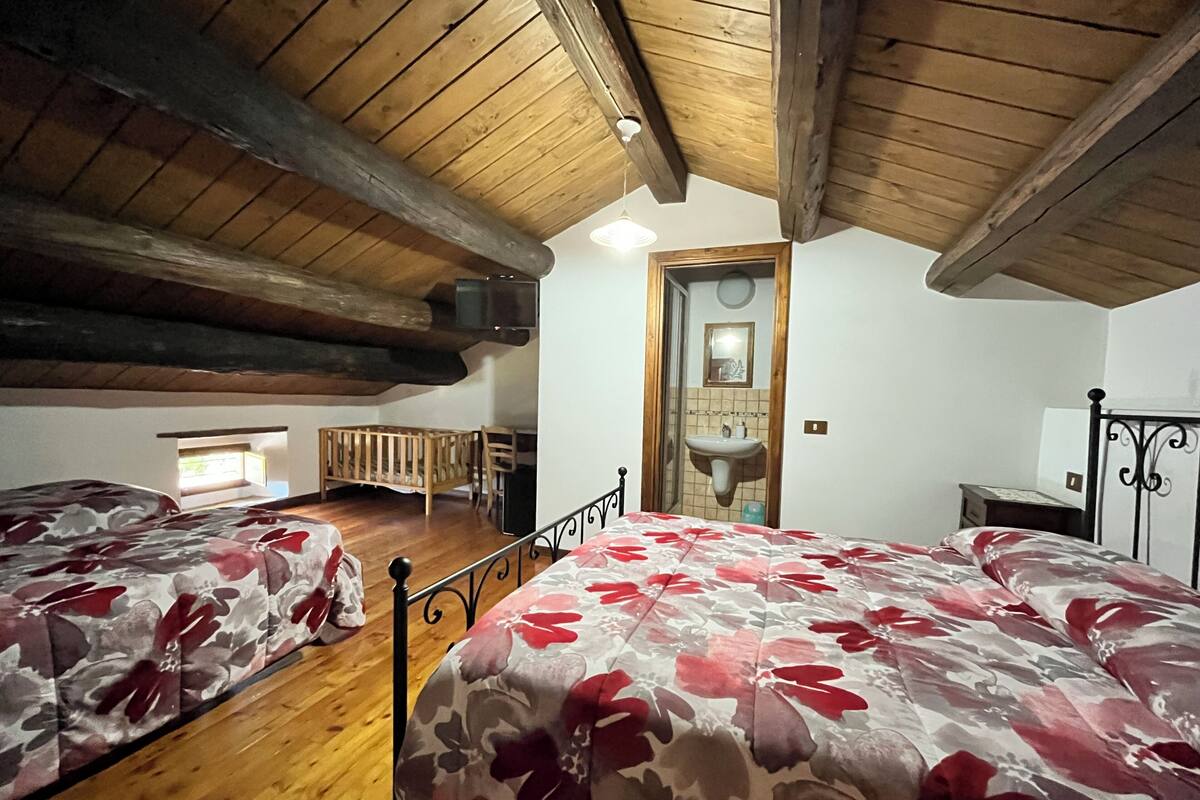 A room with two beds, wooden beams on the ceiling, a small window, and a sink.