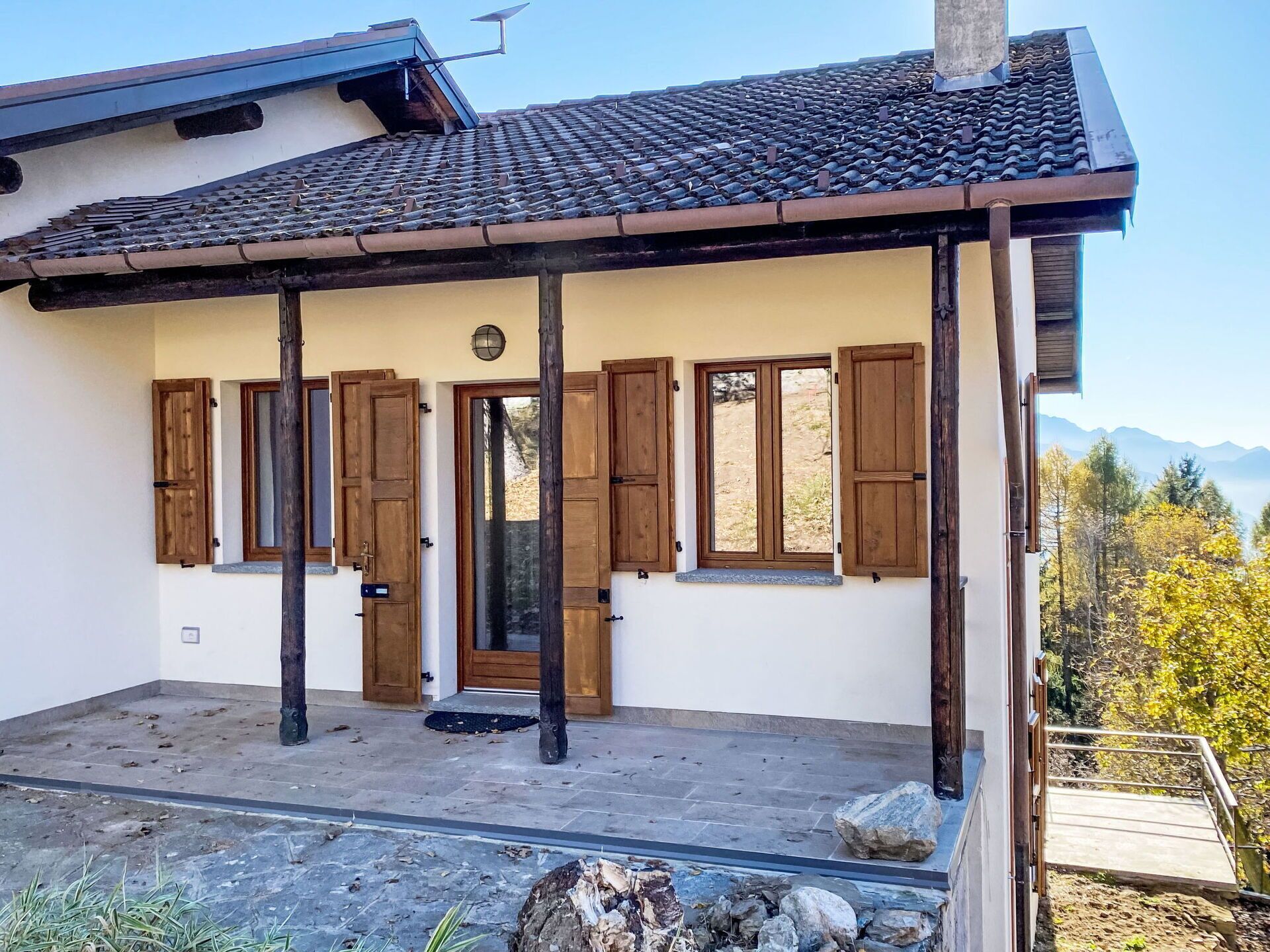 A building with a tiled roof, wooden shutters, a stone-paved entrance, and a view of mountains.