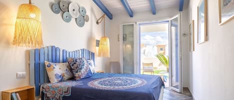 A bedroom with a bed, a wooden nightstand, a hanging light fixture, and a view of the outside.