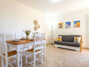 A dining area with a wooden table and white chairs, a grey sofa, and a floor lamp.