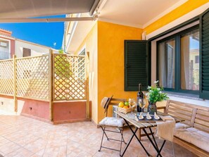 A balcony with a table set for two, a sofa, and a window with shutters.