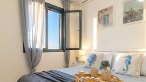 A neatly made bed with a grey bedspread, a wooden tray with cups and a 'HOME' sign, and a window with curtains.