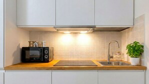A modern kitchen with white cabinets, a built-in microwave, a stainless steel sink, and a potted plant.