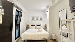 A modern bedroom with a bed, bedside tables, a mirror, and a view of the outside. - ZUR Boutique Hostel (Fuengirola)
