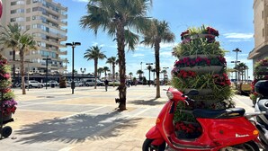 A red scooter parked on a paved area with palm trees and a building in the background. - ZUR Boutique Hostel (Fuengirola)